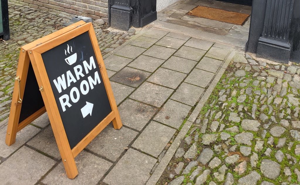 A street scene featuring an A-board saying WARM ROOM, with an arrow pointing to a building.